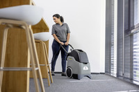 Person using a Kärcher carpet cleaner in a modern indoor setting with wooden furniture and large windows.