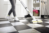 Person cleaning tiled floor with Kärcher floor cleaner, near a shoe rack and lamp in a hallway.