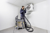 Person using Kärcher high-pressure cleaner on ceiling-mounted fan in a white indoor room.