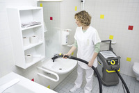 Person cleaning bathroom sink with Kärcher steam cleaner, surrounded by shelves with toilet paper and a soap dispenser.