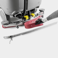 A gloved hand adjusts a red squeegee on a Kärcher floor scrubber, with a metal strip placed in front.