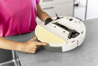 Person in pink shirt holding a robotic vacuum cleaner, showing its underside with a yellow-striped cleaning pad.