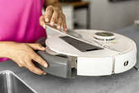 Person in pink shirt removing dust container from a white Kärcher robot vacuum on a grey countertop.