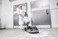 Person operating a Kärcher floor scrubber in a tiled industrial kitchen, with soap suds visible on the floor.