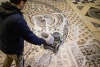 Person operating a floor cleaning machine on a decorative mosaic tile floor indoors.