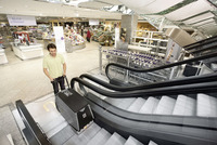 Person operating a Kärcher escalator cleaner in a busy shopping centre, with trolleys and various products visible in the background.