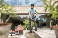 Man using Kärcher high-pressure cleaner on patio steps outside modern house.