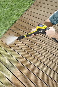 Person using a Kärcher high-pressure cleaner to wash a wooden deck next to a grassy area.