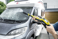 Person using a Kärcher high-pressure cleaner to wash the front window of a motorhome parked outdoors.