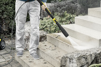 Person cleaning outdoor stone steps with a Kärcher high-pressure cleaner, surrounded by plants and rocks.