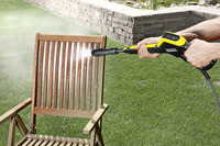 Person using a Kärcher high-pressure cleaner to wash a wooden garden chair outdoors, with water spray visible.