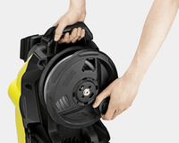 Hands adjusting the hose reel on a Kärcher high-pressure cleaner, showing the black and yellow device in close-up.