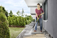 Person using a Kärcher high-pressure cleaner on a stone patio, surrounded by greenery and modern buildings.