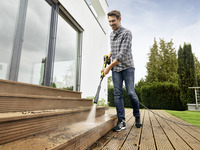 Man cleaning wooden deck steps with Kärcher high-pressure cleaner outdoors near modern house.