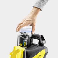 Hand placing Kärcher car shampoo bottle on a Kärcher device with a yellow compartment and black handle.