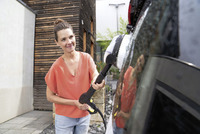 Person in orange top using Kärcher high-pressure cleaner on a car outdoors, near a wooden building.
