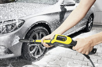 Person using a Kärcher high-pressure cleaner to wash a silver car, with soap suds covering the vehicle's surface.