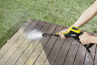 Person using a Kärcher high-pressure cleaner on a wooden deck, with grass visible in the background.