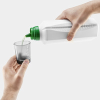 Hands pouring liquid from a white bottle with a green cap into a measuring cup.