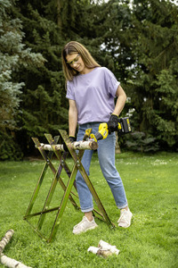 Person using a Kärcher chainsaw to cut a log on a metal sawhorse in a grassy outdoor setting surrounded by trees.