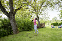 Person using a Kärcher pole saw to trim tree branches in a garden, surrounded by greenery and outdoor furniture.