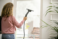Person using a Kärcher window vac to clean a glass door indoors, with a view of a tiled roof outside.