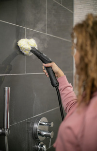 Woman using Kärcher steam cleaner on bathroom tiles.