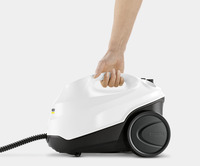 Hand holding a white Kärcher steam cleaner with black wheels and a coiled cord on a light grey background.