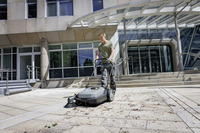 Person using a Kärcher floor sweeper on a tiled outdoor area in front of a modern building with large windows and steps.