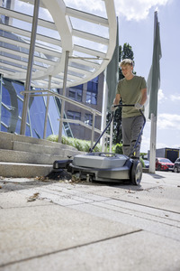 Person using Kärcher floor sweeper outdoors near building entrance with glass canopy and steps.