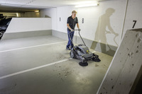 Person using a Kärcher floor sweeper in an indoor car park, cleaning debris from the concrete floor near parking spaces marked 7, 8, and 9.