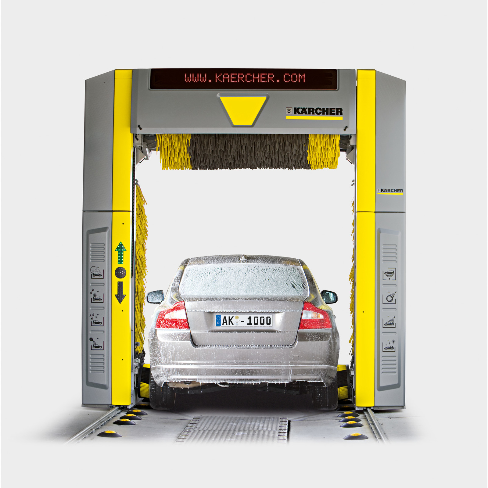 Mașină argintie spălată într-un sistem automat Kärcher, acoperită cu spumă, în interiorul unei spălătorii auto.