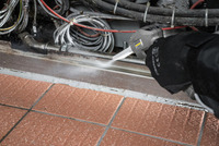 Gloved hand using Kärcher steam cleaner on tiled floor near cables and pipes.