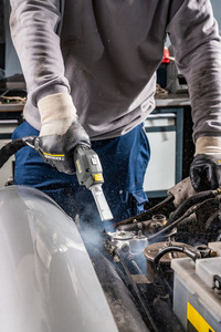 Person using a Kärcher high-pressure cleaner on a car engine in a garage, wearing gloves and a grey sweatshirt.