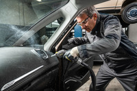 Person cleaning car interior with Kärcher steam cleaner in a garage setting, focusing on the dashboard area.