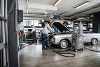 Mechanics working in a garage on a silver convertible car with a Kärcher cleaning machine in the foreground and a car lift in the background.