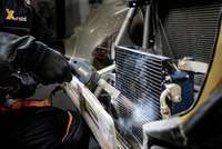 Person cleaning a radiator with a Kärcher high-pressure cleaner in a garage setting.