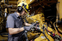 Worker in protective gear using a Kärcher high-pressure cleaner on industrial machinery, surrounded by cables and hydraulic components.
