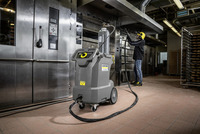 Worker using Kärcher professional cleaning equipment in an industrial kitchen, with ovens and baking trays visible.