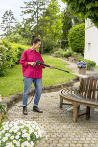 Person in red shirt using Kärcher high-pressure cleaner on wooden bench in a garden setting with lush greenery and flowers.