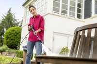 Person in red shirt using Kärcher high-pressure cleaner on wooden outdoor furniture, with house and garden in background.