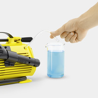 Hand holding a tube from a Kärcher high-pressure cleaner, inserting it into a beaker filled with blue liquid.
