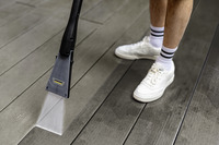 Kärcher high-pressure cleaner spraying water on a wooden deck, next to a person wearing white trainers and striped socks.