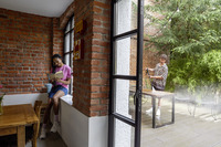Person reading indoors by a brick wall, while another uses a Kärcher high-pressure cleaner on a wooden table outside.