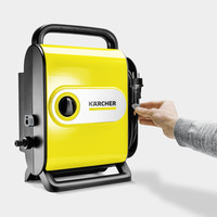 Hand plugging in the power cord of a yellow Kärcher high-pressure cleaner against a grey background.