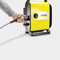 Hand connecting a hose to a yellow Kärcher high-pressure cleaner against a plain background.