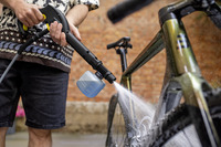 Person cleaning a bicycle with a Kärcher high-pressure cleaner, spraying water on the frame outdoors near a brick wall.