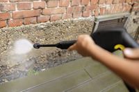 Person using a Kärcher high-pressure cleaner to spray water on a brick wall outdoors.