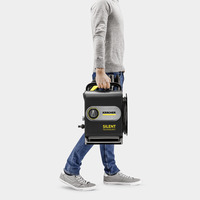 Person in grey jumper and jeans carrying a Kärcher Silent Technology high-pressure cleaner.