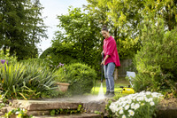 Person using Kärcher high-pressure cleaner on garden steps, surrounded by lush greenery and blooming flowers.